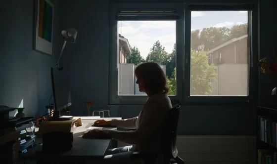 Margreet in silhouet aan haar bureau, voor het raam